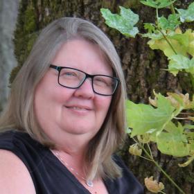 A woman in a black shirt with glasses on smiling