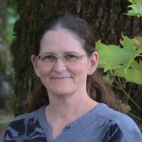 A picture of a woman with glasses and a blue/grey shirt smiling